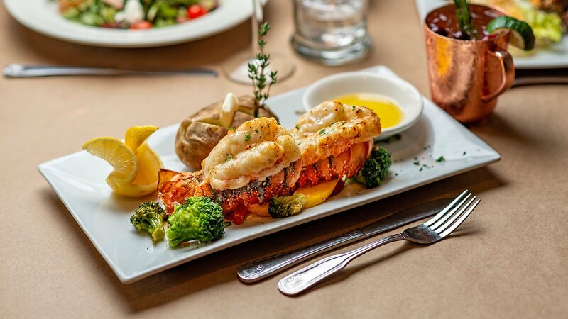 Twin lobster tails entree with side of baked potato, vegetables and melted butter